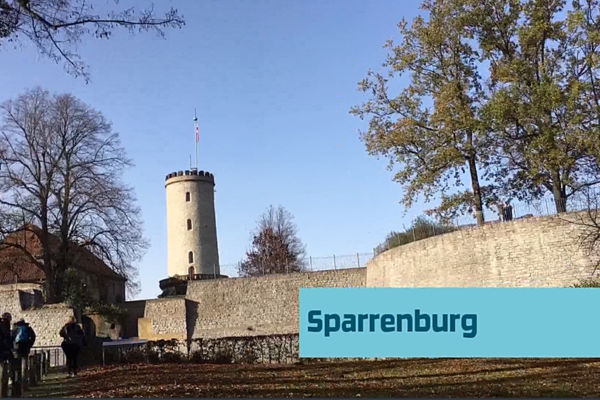 Foto der Sparrenburg in Bielefeld. Hinter einer Steinmauer ragen ein Turm und mehrere Bäume hervor.