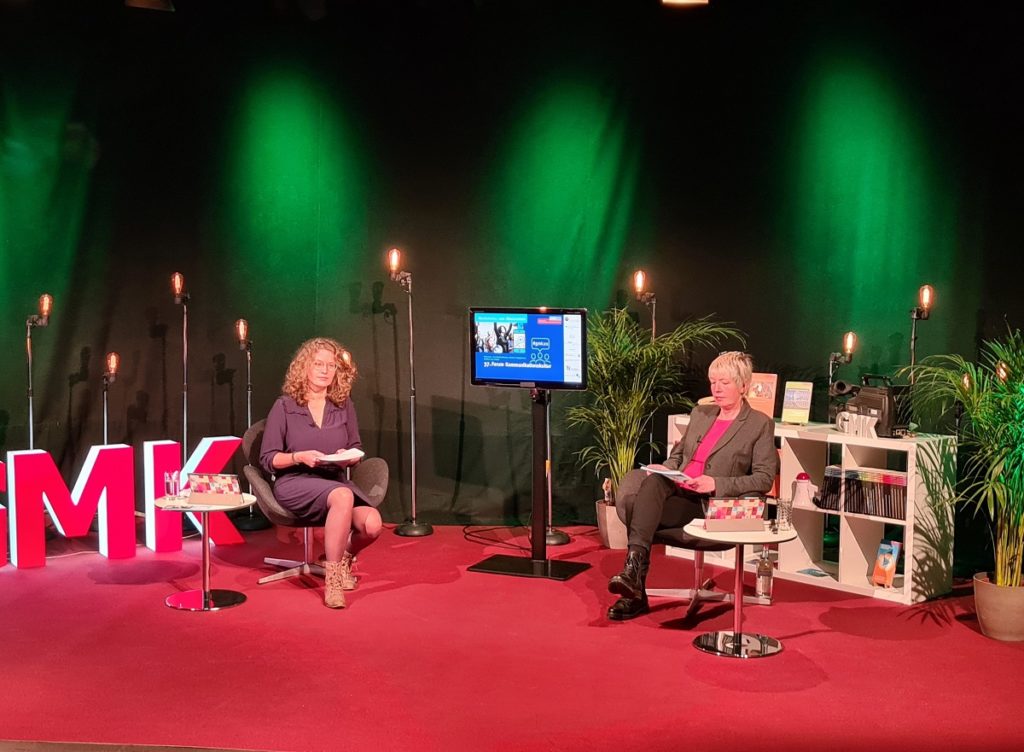 Foto des Studios des Forums Kommunikationskultur 2020. Im Studio sitzen Anja Pielsticker und Andrea Marten. Zwischen ihnen ist ein Fernsehbildschirm aufgebaut.