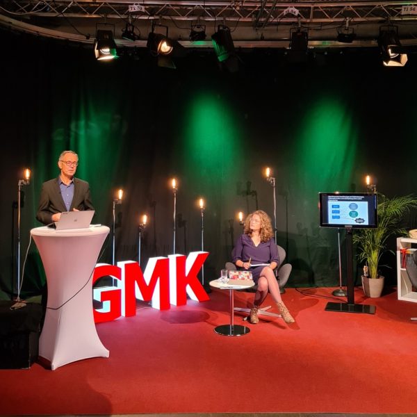 Foto des Studios des Forums Kommunikationskultur 2020. Im Studio sitzen Anja Pielsticker und Andrea Marten, welche Andreas Zick zugewandt sind, der an einem Stehtisch neben ihnen steht und spricht.