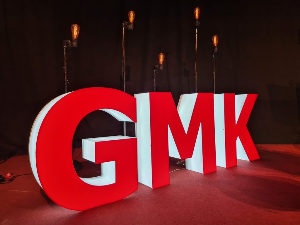 Initialen der GMK als dreidimensionale, weiß leuchtende Großbuchstaben mit roter Front