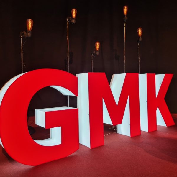 Initialen der GMK als dreidimensionale, weiß leuchtende Großbuchstaben mit roter Front