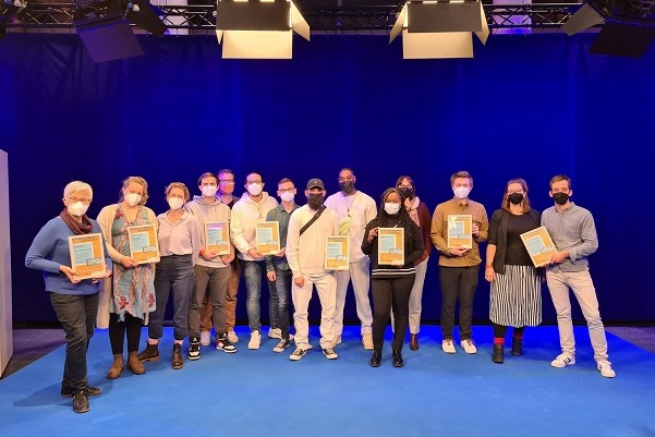Gruppenfoto der Preisträger und Preisträgerinnen des Dieter Baacke Preises 2021, sie stehen vor einem Blue Screen und präsentieren ihre Urkunden