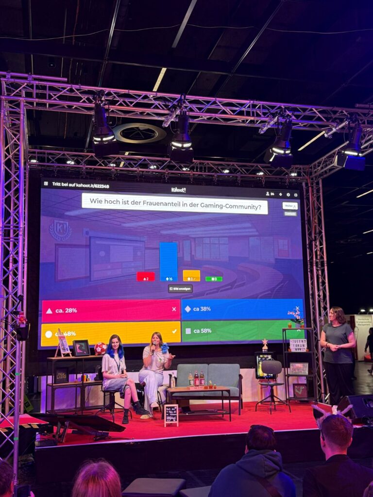 Zwei Personen sitzen auf der Bühne und sprechen über das im Hintergrund dargestellte Ergebnis einer Umfrage zum Frauenanteil in der Gaming-Community